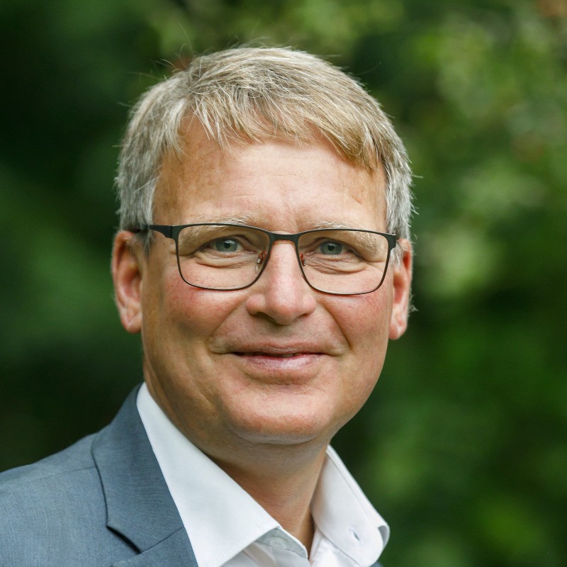 A portrait photo of a man wearing a grey suit, glasses and looking straight at the camera.
